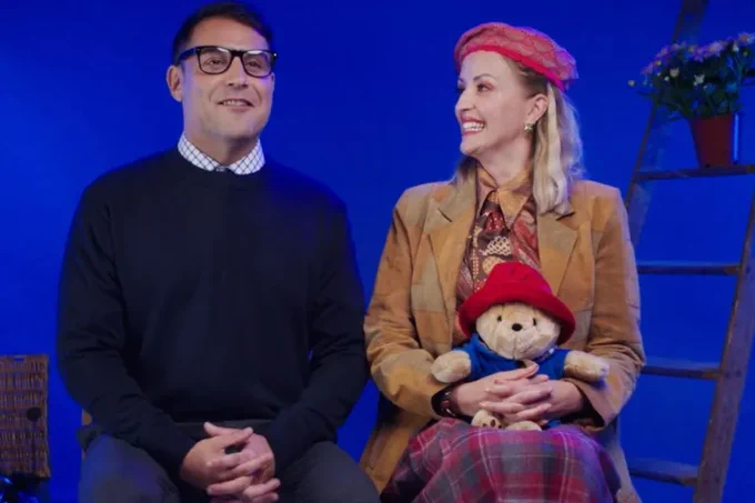 Two performers smile together holding a Paddington Bear teddy