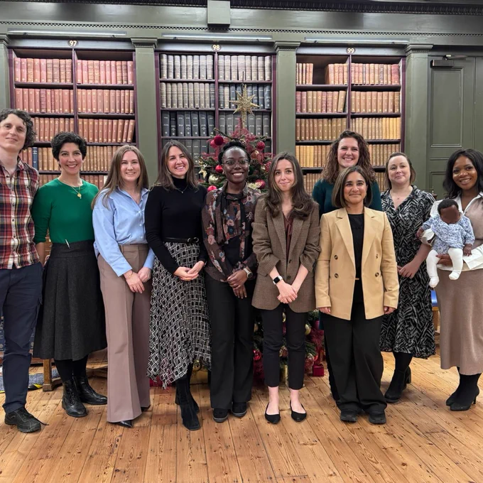 Group of ten adults standing in front of a decorated Christmas tree and tall bookshelves filled with old books at a previous Emerging Leaders event. 