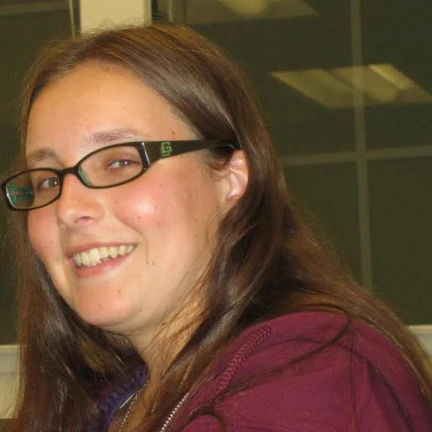 Candid photo of a female with really long brown hair, dark colored glasses, wearing a dark maroon sweatshirt.  