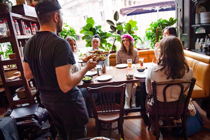 Member of staff serving food to a group of people sitting at a table in a restaurant. VisitBritain/Nemorin