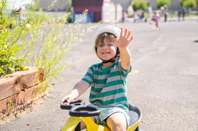student waves as he is riding on a toy vehicle