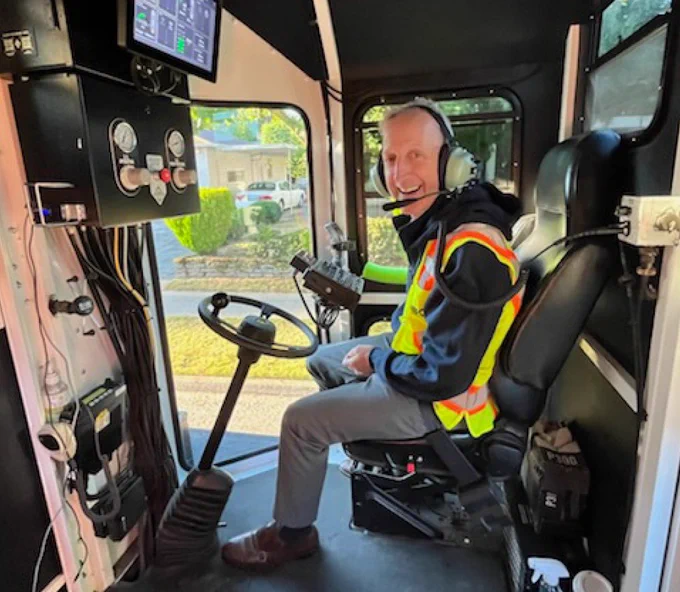 Mayor Wilson riding in the front of a Portland Bureau of Transportation striping truck while wearing a headset and yellow safety vest.