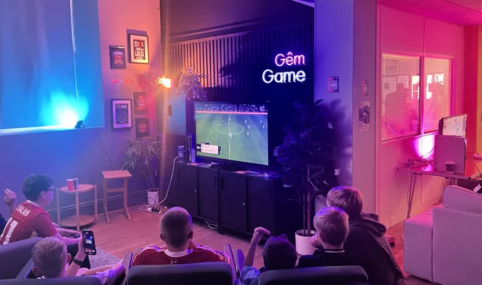 Young people sat on chairs and sofas, playing video games.