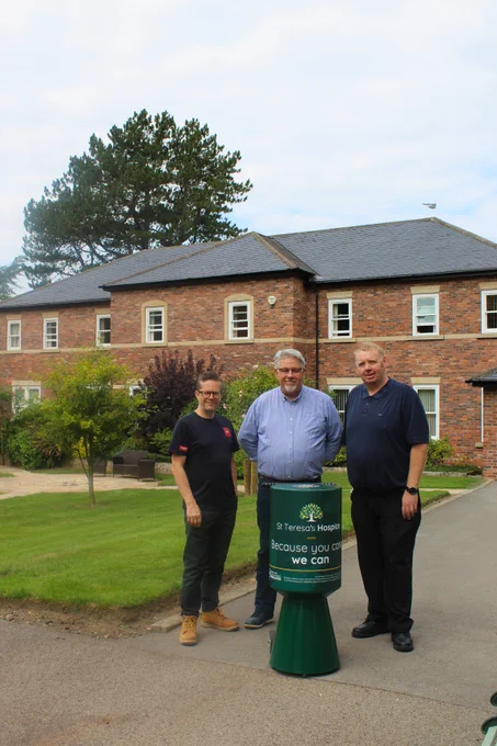 From left: Keiran Bayley from Intake VHQ, Andrew Fisher from Fab Shop and Paul Dyke from Cummins. The three men are standing with a giant green collection tin which has a giant 'St Teresa's Hospice' label on it. The photo is taken in the picturesque hospice gardens.