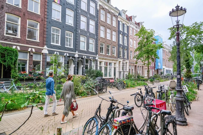 People of all ages and abilities walk, cycle, sit, and socialise along the residential streets of Amsterdam, which are lined with buildings, trees, flowers and plantings, benches, and terraces.