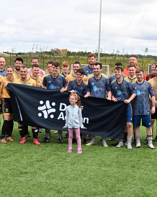 A football team all standing together holding a flag with text overlaid reading "Deaf Action". In front of them is a small girl smiling.
