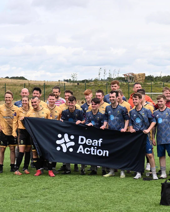 A football team all standing together holding a flag with text overlaid reading "Deaf Action".