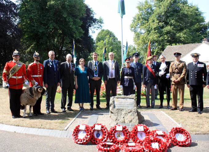 A line of people, several in military uniform, standing behind a ceremonial stone on which wreaths have been laid.