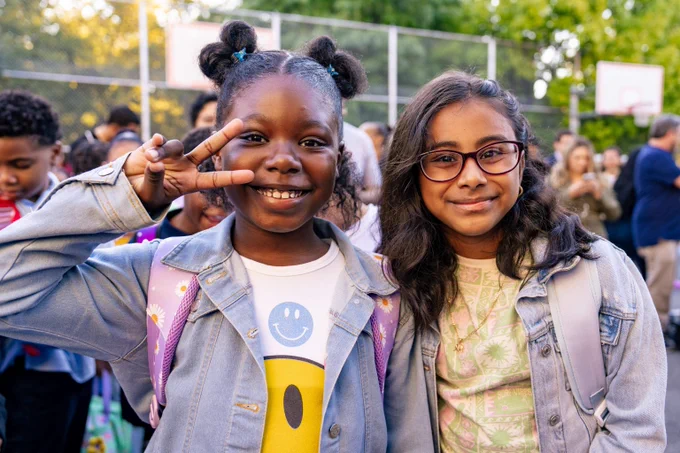 Two students smile outside on the first day of school in 2024. One student is holding up a peace sign.