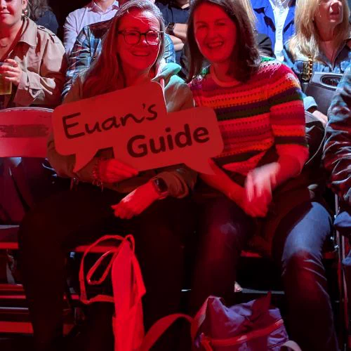 I'm of Antonia and Kiki from Euan's Guide. They set under red stage lights holding a Euan’s Guide sign