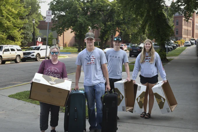 four people smiling at camera holding boxes and luggage