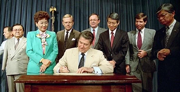 Reagan signing the Civil Liberties Act of 1988. He is surrounded by Hawaii Sen. Spark Matsunaga, California Rep. Norman Mineta, Hawaii Rep. Pat Saiki, California Sen. Pete Wilson, Alaska Rep. Don Young, California Rep. Bob Matsui, California Rep. Bill Lowery, and JACL President Harry Kajihara. Photo courtesy of Ronald Reagan Presidential Library.