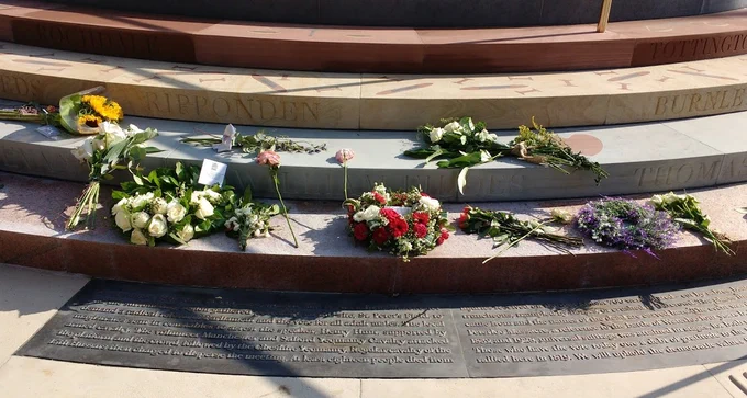 Wreaths and bunches of flowers lying on the bottom two levels of the Peterloo memorial, above the inscription telling the story of the Peterloo massacre and why we should remember it.