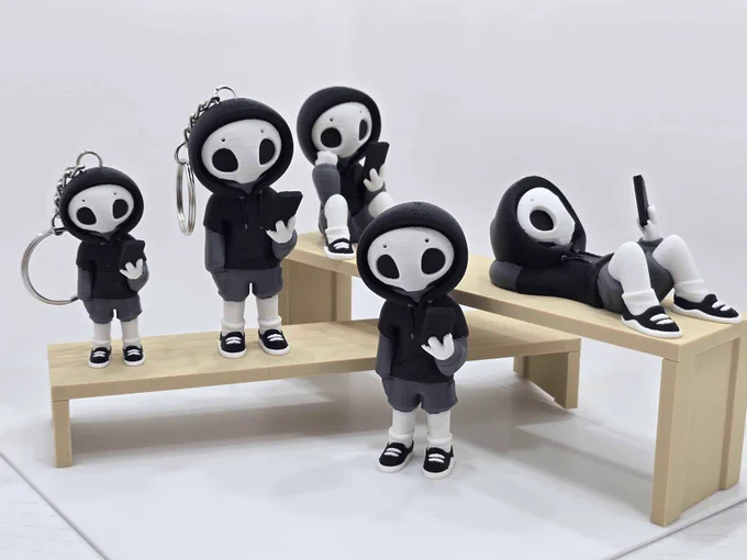 Five hooded “Project Hazy” figures, two as keychains, posed on a beige 3D printed bench set, with one figure lying down and looking at their phone.