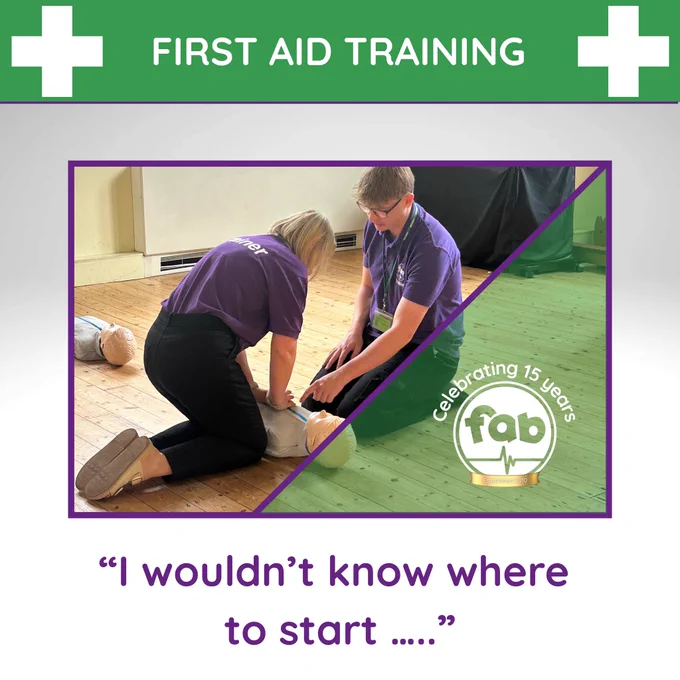 A blond female kneeling beside a junior manikin demonstrating the CPR position wearing a purple fabtraining polo shirt and black trousers being instructed by a male with light brown hair and glasses kneeling opposite wearing the same uniform. 