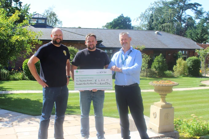 Three men holding a cheque - one wearing a St Teresa's Hospice lanyard - in the hospice gardens.