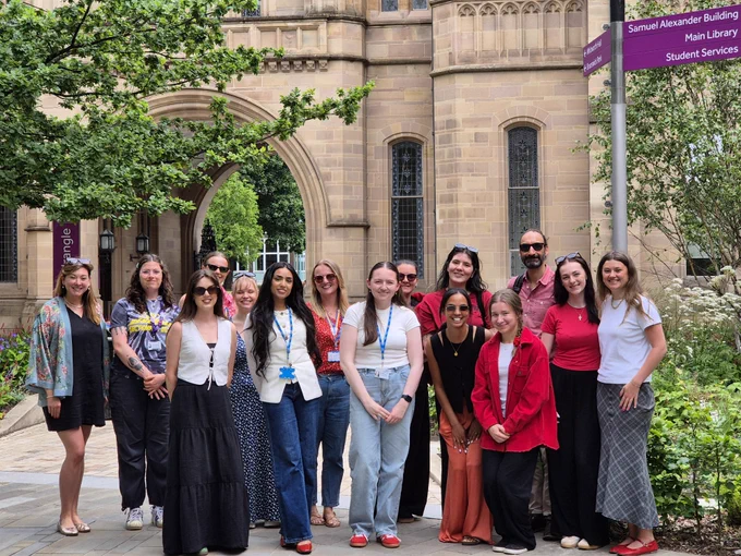 Fifteen people standing in front of a Manchester University building