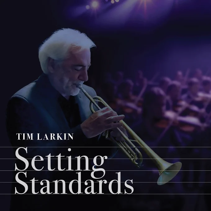 An album cover of Tim Larkin playing trumpet in a dark and moody stage performance setting with a blurred orchestra behind him. The text reads "Tim Larkin" "Setting Standards".