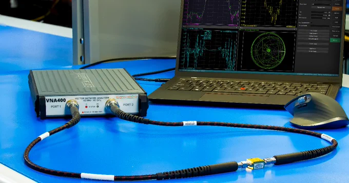 A Signal Hound Vector Network Analyzer (VNA) connected by cables to a laptop displaying technical graphs and radar data.
