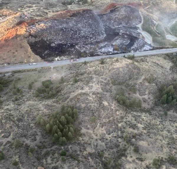 A line of fire retardant is visible on a grassy hillside above a roadway