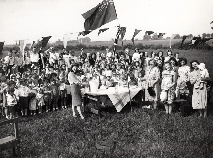black and white photo of a group of people having a picnic in a field surrounded by bunting and flags