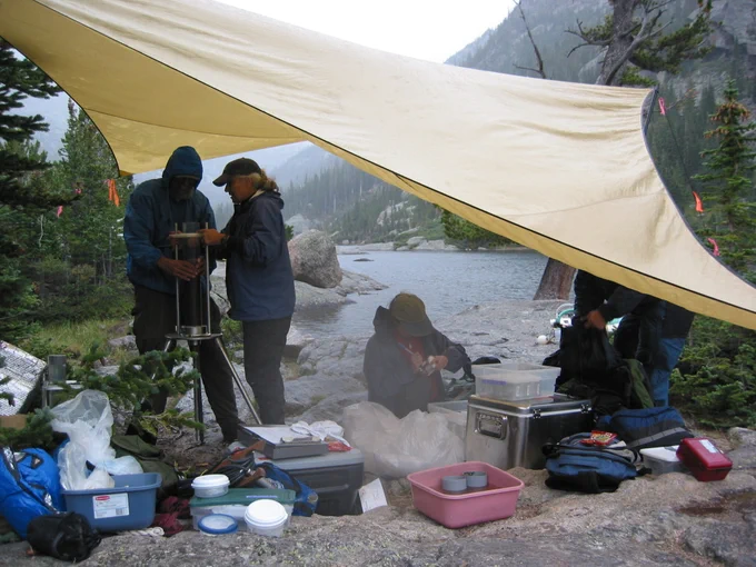 People working under a tent next to a river.