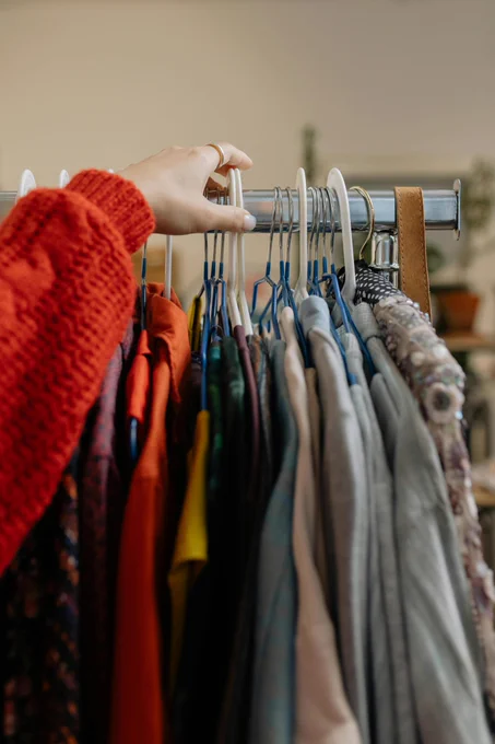 Someone in a red sweater reaches to a clothing rack with assorted clothing. 