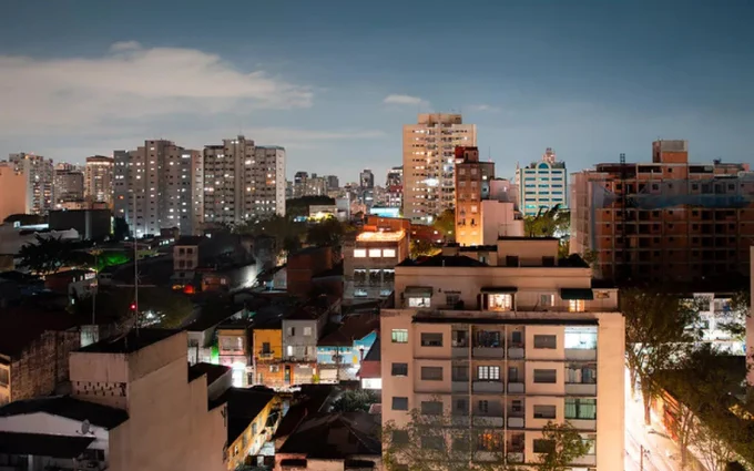 Nighttime view of a densely populated urban area with illuminated buildings against a dusky sky.