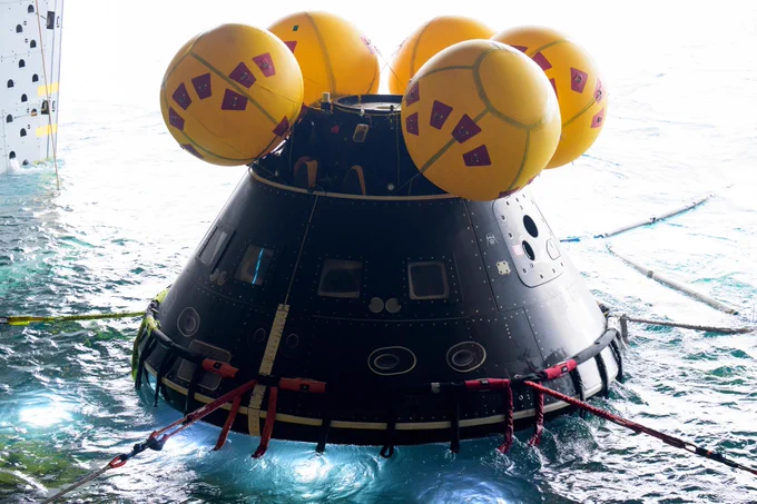 A full scale mockup of the Orion spacecraft is seen during Underway Recovery Test-12 onboard USS Somerset off the coast of California, Mar. 26, 2025. The spacecraft has dark gray paneling, four yellow inflatables attached to the top, and is seen floating in the water. Credit: NASA/Bill Ingalls