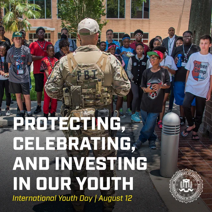 FBI agent in tactical gear addressing a diverse group of youth outdoors near a brick building on International Youth Day. The FBI seal is in the corner.