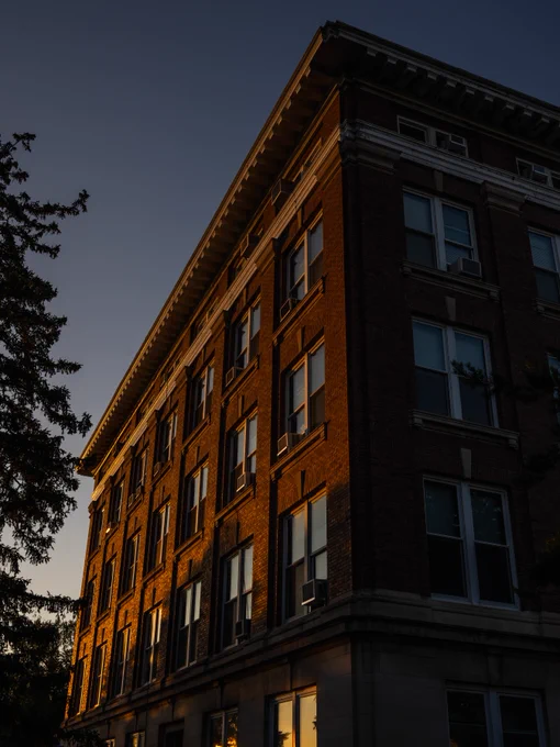A red brick building with a corner turret is bathed in the warm light of the setting sun.