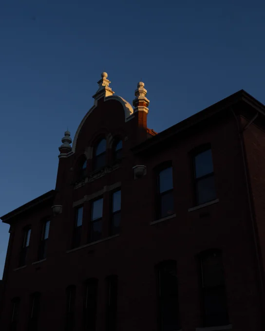 A historic brick building with with a curved roof and detailing is silhouetted against a blue sky at sunset.