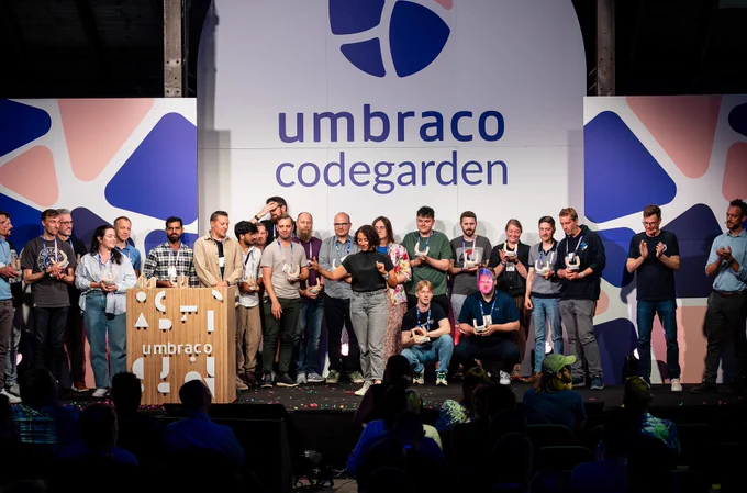 A diverse group of award recipients stands on stage at the Umbraco Codegarden conference, each holding a trophy. A large Umbraco logo and the word “codegarden” are displayed on the backdrop. The mood is celebratory, with some people smiling and others clapping.
