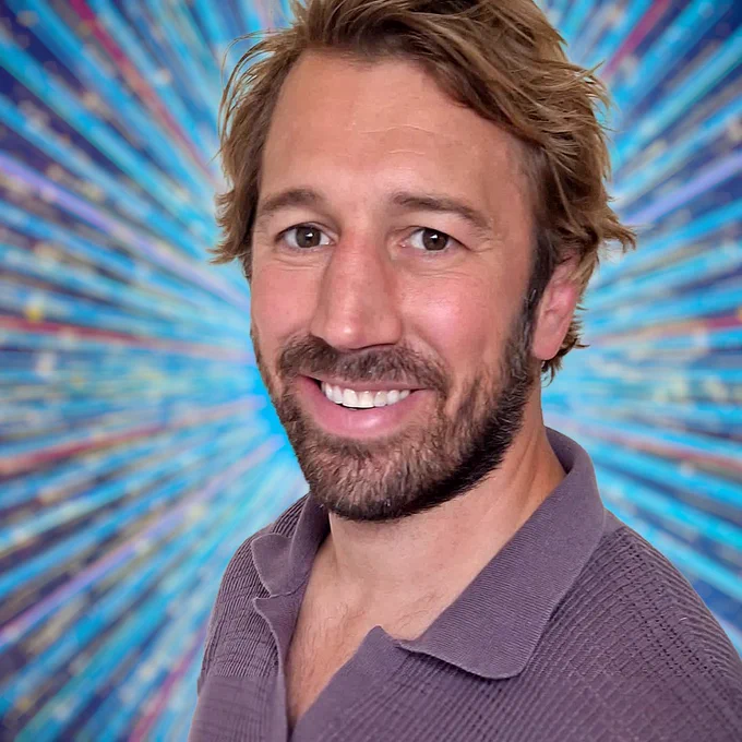 A head and shoulders shot of Chris Robshaw, smiling to camera in a grey/brown polo shirt against a glittering blue background
