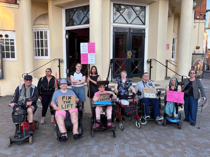 A group of Disabled people gathered outside New Wimbledon Theatre in Wimbledon. 