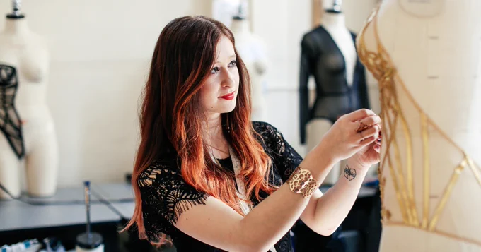 A fashion designer adjusting a dress on a mannequin in a studio with other mannequins in the background.