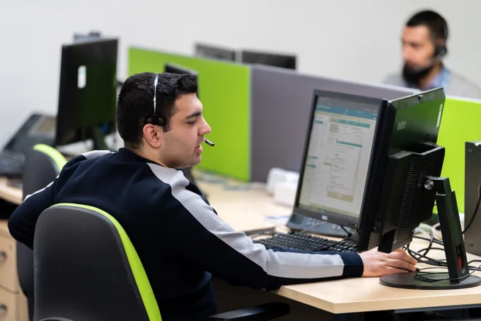 Customer service representative wearing a headset working on a desktop computer in a modern office cubicle.