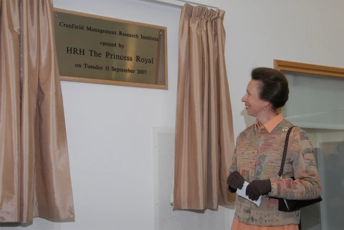 Princess Anne standing beside the plaque she had just unveiled. There are open orange curtains either side of the plaque and she is facing towards it.