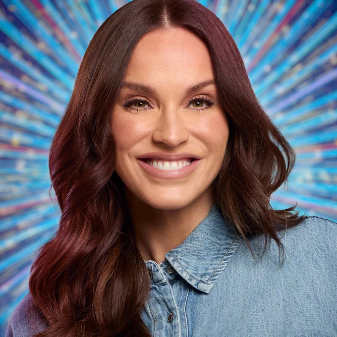 Vicky Pattison smiles to camera wearing a blue denim shirt, set against a glittering blue backdrop