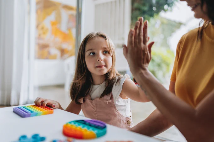 A young girl hi-fiving an adult, while playing with a colourful toy