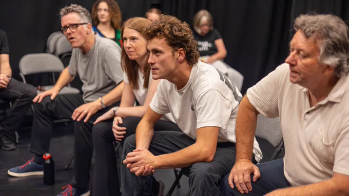 Exe Men rehearsal photo. Four cast members sit in a row, gazing intensely ahead.
