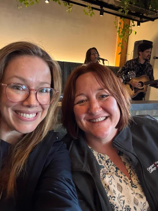 Smiling selfie of two participants of the Casper/Edmonton exchange, with two band performers in the background.
