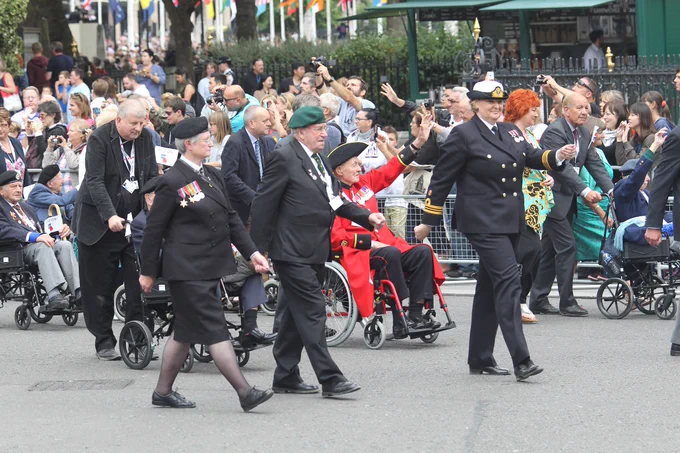 Veterans smiling and waving to crowds gathered to cheer them on as they march to Westminster Abbey