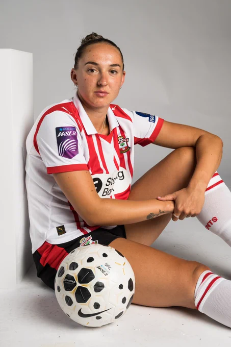 Aimee Palmer sits next a Women's Super League match ball, wearing the red and white home kit.