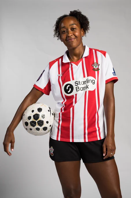 Atlanta Primus poses with a Women's Super League match ball under her arm, wearing the red and white home kit.