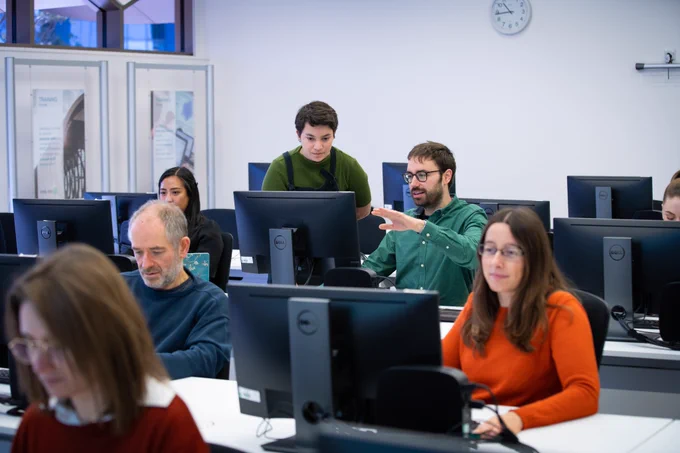 A group of people look at computer screens in a computer lab. 