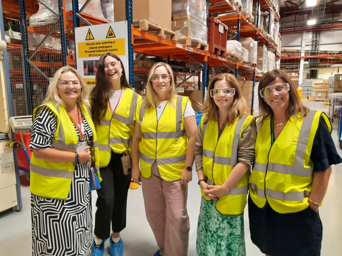A group of Abbott and TCPID colleagues standing in the warehouse in Abbott Sligo. All are wearing yellow hi-vis jackets, safety glasses and blue shoe covers