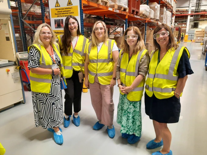 A group of Abbott and TCPID colleagues standing in the warehouse in Abbott Sligo. All are wearing yellow hi-vis jackets, safety glasses and blue shoe covers