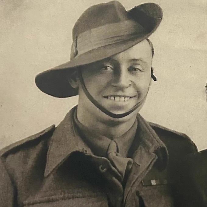 An image of a black and white photo of Tom smiling at the camera, wearing military uniform and a hat.