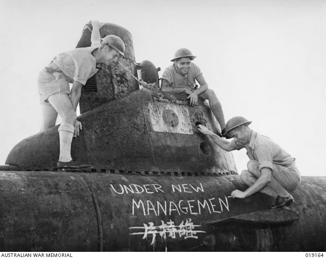 Crew members of HMAS Napier chalk a sign that reads ‘under new management’ on a Japanese midget submarine, Azuma Peninsula, Tokyo Bay, Japan, September 1945. Reference: Australian War Memorial 019164.